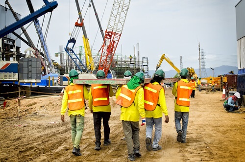 construction workers carrying beam on construction site
