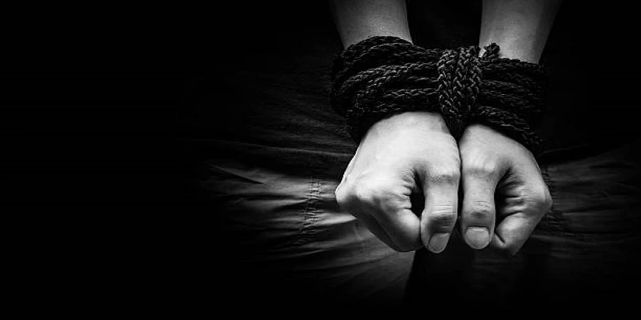 A black and white image of a person's hands tied together with rope in front of them.