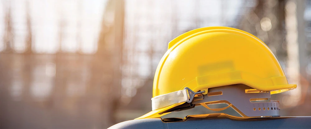 A yellow hard hat laying on top of a metal barrier at a construction site.