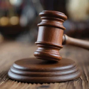 A dark wood gavel on a textured wooden surface, laying still after a verdict has been reached.