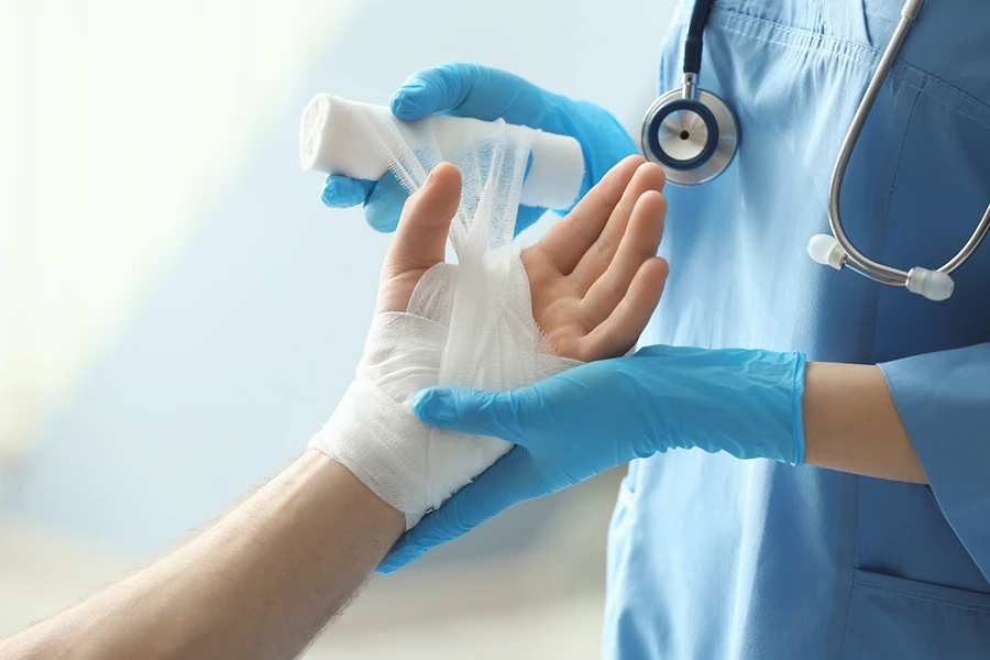 doctor in blue scrubs wrapping a fabric bandage around patient's hand