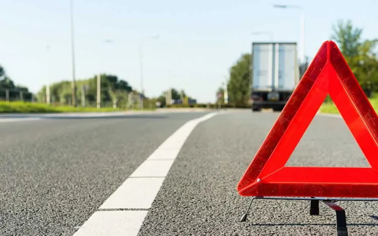 Triangle reflective hazard sign with broken down truck in the background