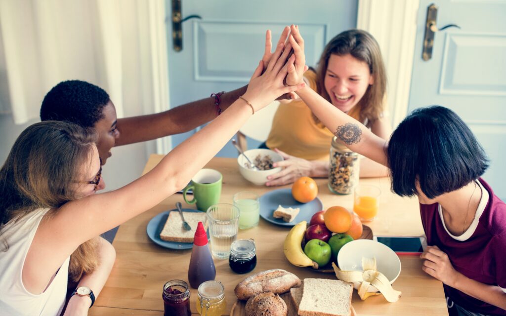 Diverse group of young adult women seated around a breakfast table, high-fiving.