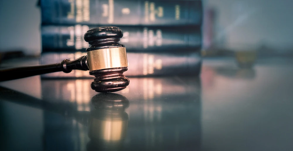 A judge's gavel on a lightly reflective table in front of a stack of legal books.
