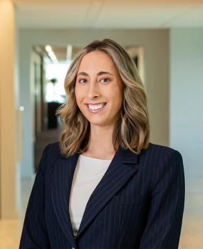 Professional woman in a navy pinstripe blazer standing in a bright hallway, smiling toward the camera, businesslike portrait.
