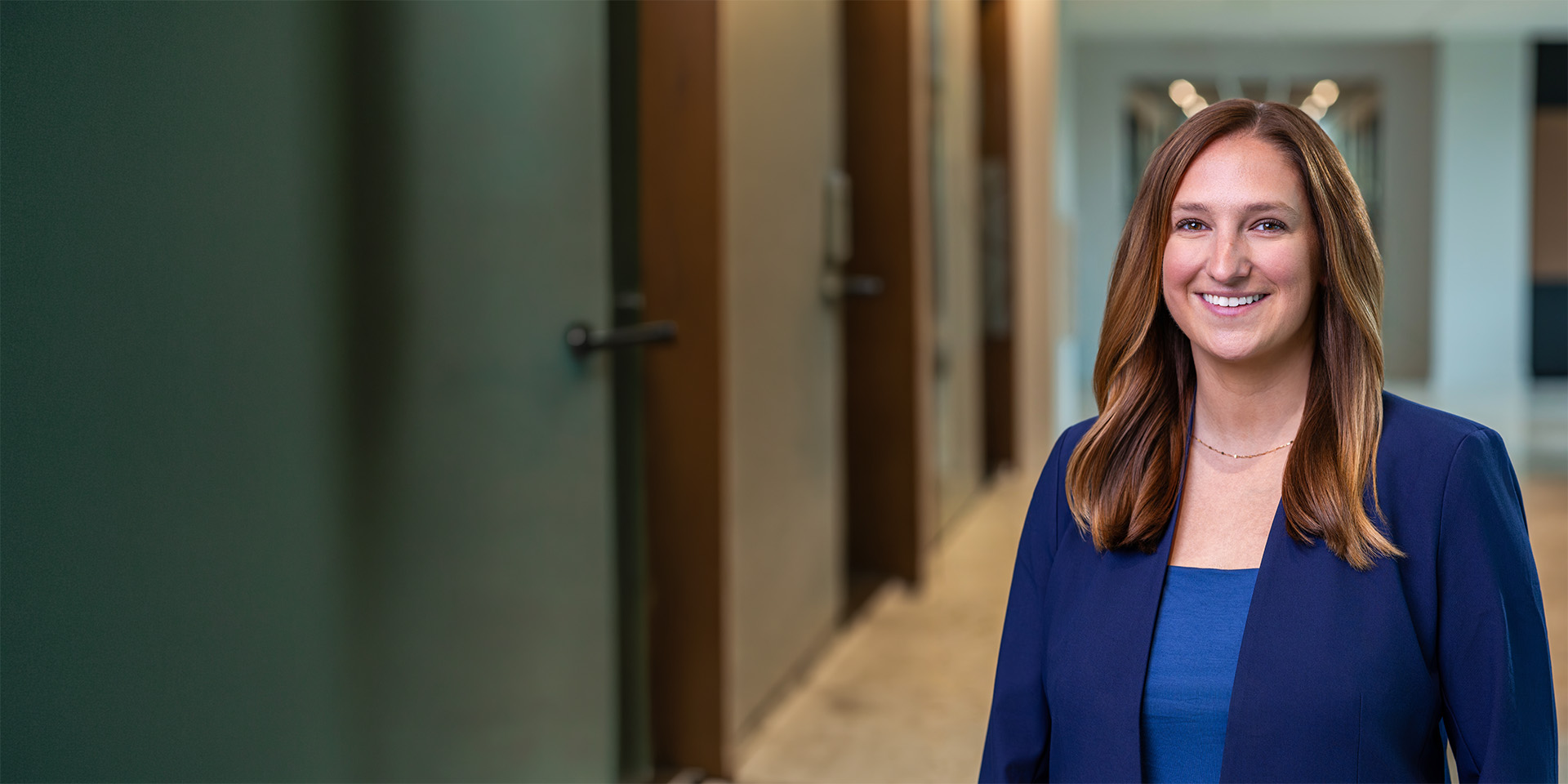 Smiling woman in a blue blazer stands in a modern office hallway