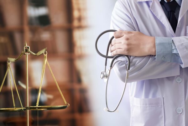Doctor holding a stethoscope standing next to the Scales of Justice