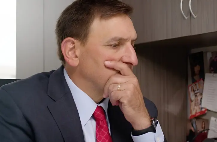 Anthony sitting at his desk with his hand on his face, thinking.