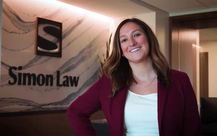 Smiling woman in a burgundy blazer stands in a law office lobby with a marble-pattern wall and 'Simon Law' sign behind her.