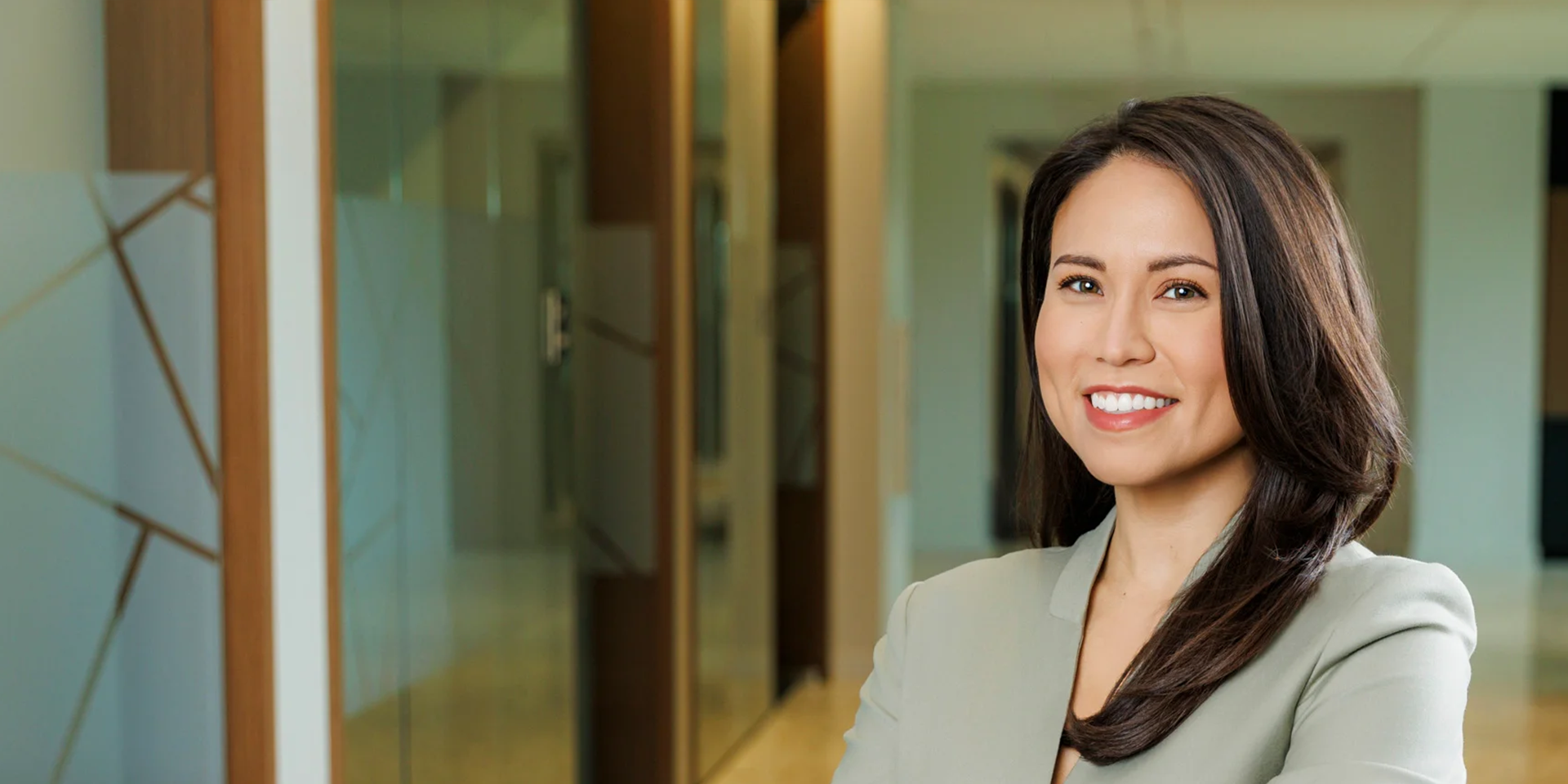 Smiling woman in a light blazer standing in a modern office hallway, portrait orientation.