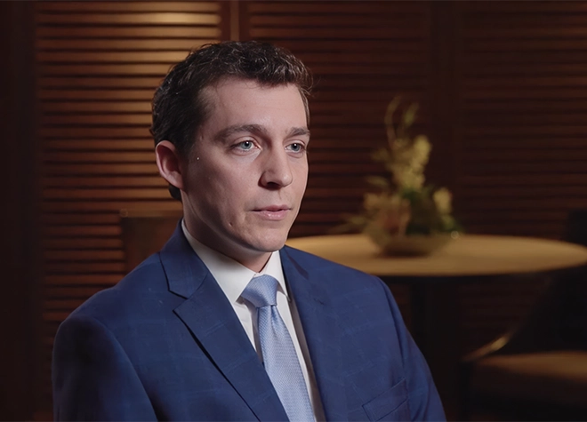 Close up of Patrick sitting in the board room being interviewed.
