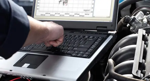 mechanic typing on a laptop with auto parts next to the laptop.