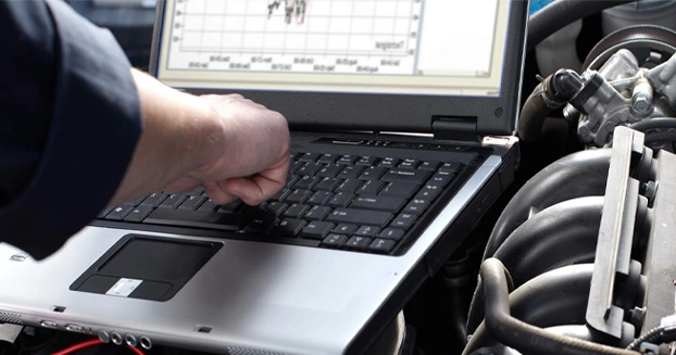 mechanic typing on a laptop with auto parts next to the laptop.