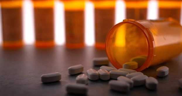 A prescription bottle spilled open with pills falling out on a table