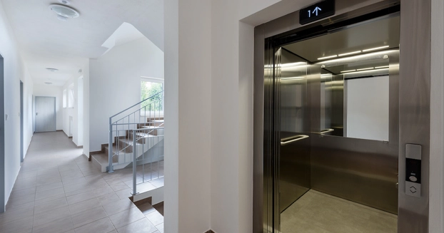 The hallway of a home with an elevator on the right and a big staircase in the background.