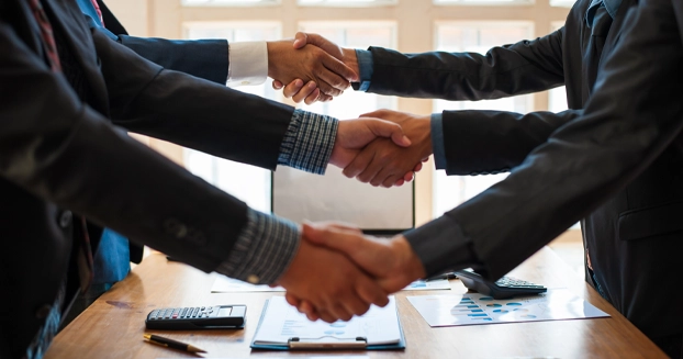 Six business men shaking hands across of a conference table.