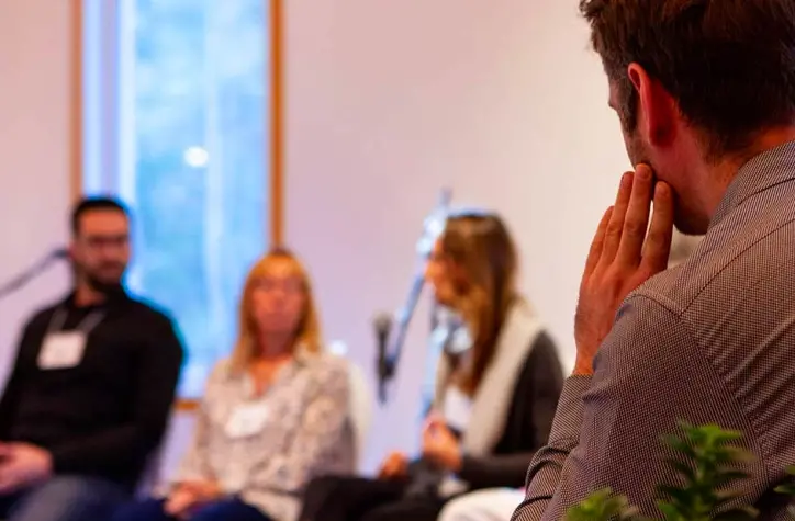 Man sitting in a seminar listening to the three speakers in front of him.