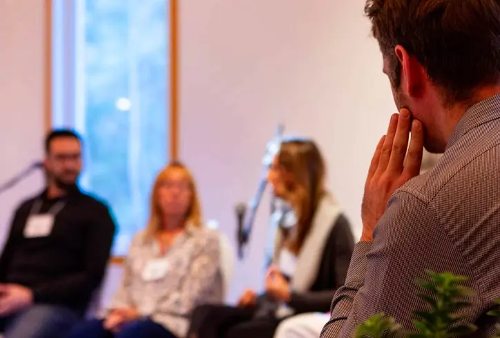 Man sitting in a seminar listening to the three speakers in front of him.