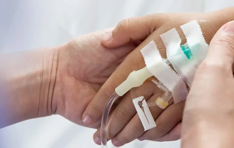 Close up of two hands holding and one hand with an IV going through the top.