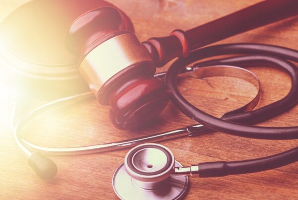 physician's stethoscope on a wooden table with a judge's gavel lying on top.