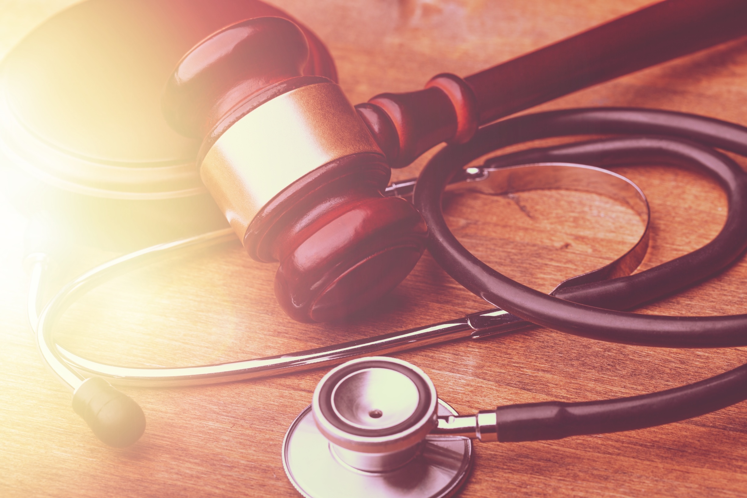 physician's stethoscope on a wooden table with a judge's gavel lying on top.