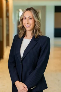 Professional woman in a navy pinstripe blazer smiling in a bright office hallway, white blouse underneath.