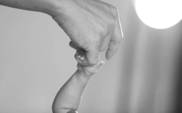 Newborn baby's hand holding finger of mother.