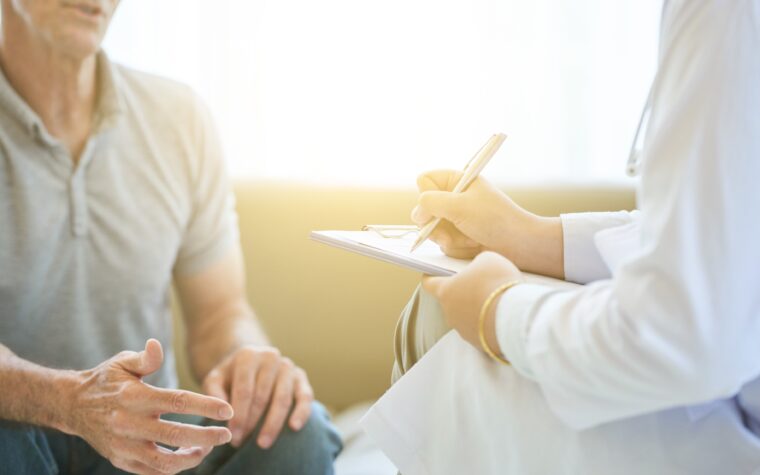 Senior man talking to doctor who is taking notes on clipboard for a second opinion