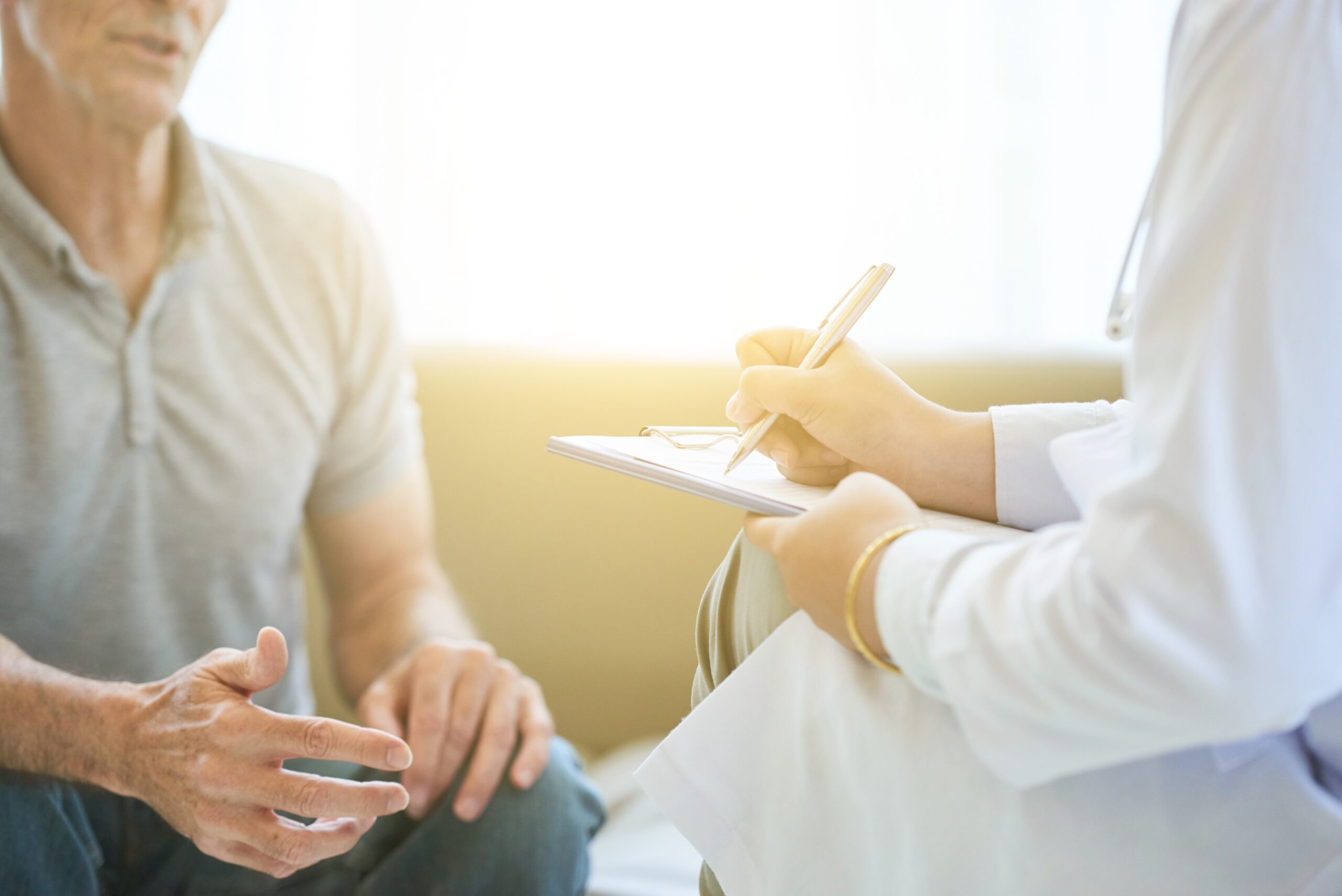 Senior man talking to doctor who is taking notes on clipboard for a second opinion