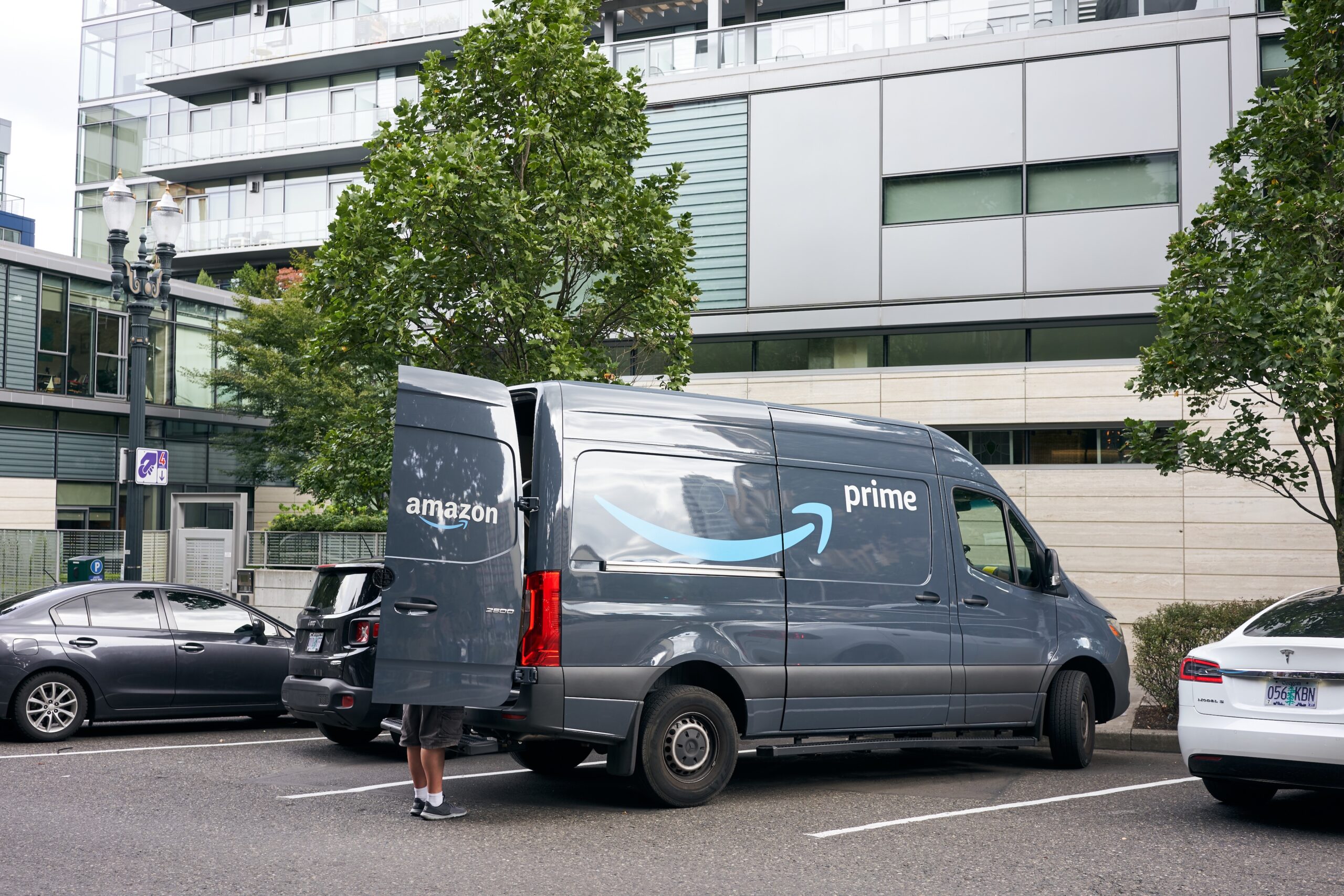 An Amazon Prime delivery van is being unloaded in a residential parking lot.