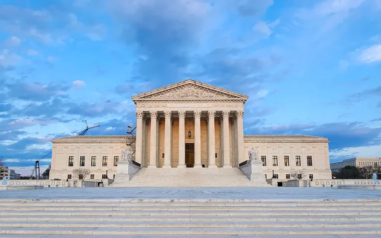 Neoclassical courthouse with tall columns and a large pediment, set on wide steps with US flags on either side under a blue sky.