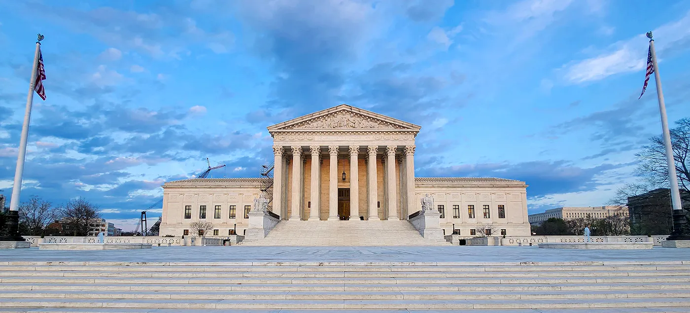 Neoclassical courthouse with tall columns and a large pediment, set on wide steps with US flags on either side under a blue sky.