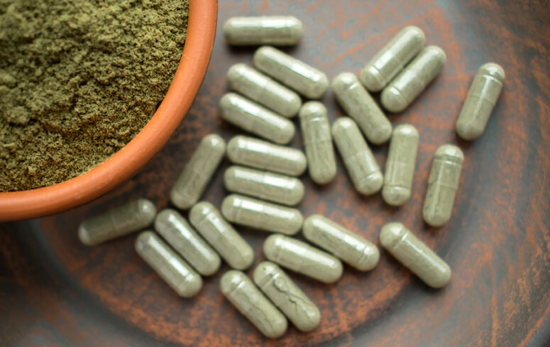 Supplement kratom green capsules and powder on brown plate. Herbal product alt-medicine kratom is opioid. Home alternative pain remedy, opioid addiction, dangerous painkiller, overdose.