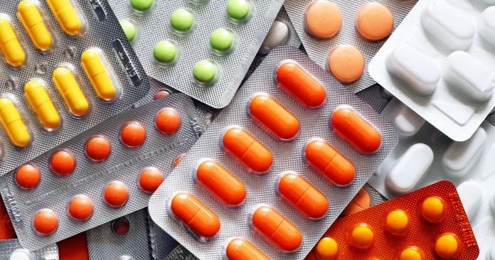 Assorted blister packs with orange capsules, yellow pills, green tablets, and white tablets